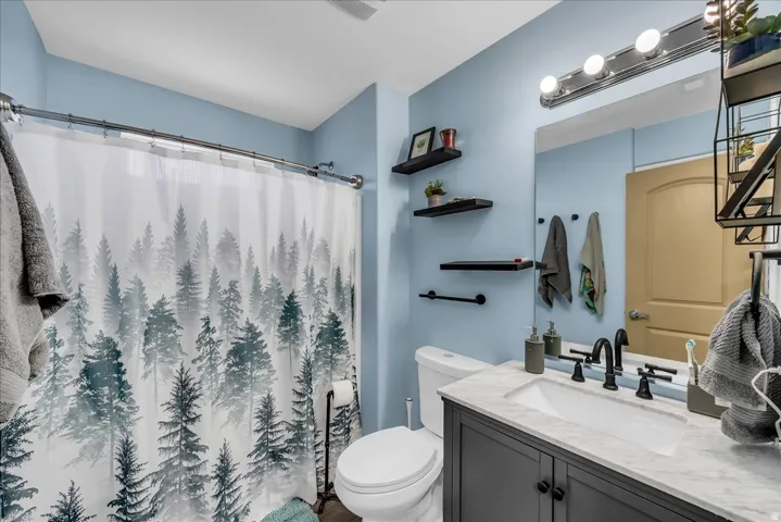Bathroom featuring a single-sink vanity with dark cabinetry, integrated lighting, wall-mounted mirror, and floating shelving