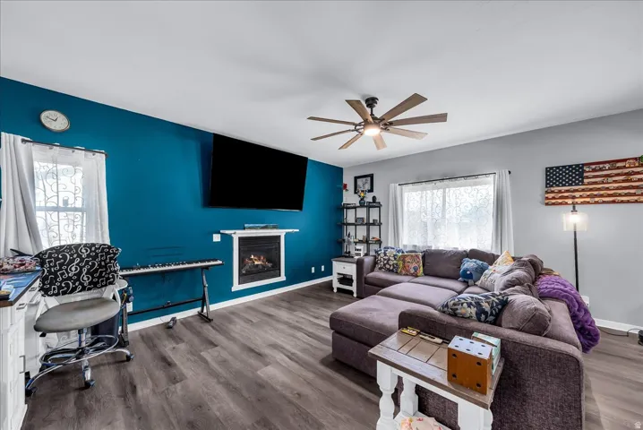 Living area featuring wood-finish flooring, a ceiling fan with integrated lighting, and a built-in fireplace with a white mantel