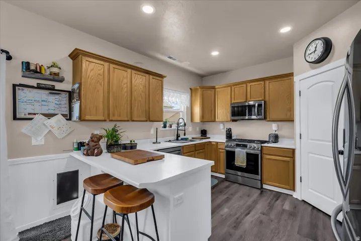 Expansive kitchen featuring wood-finish cabinetry, stainless steel appliances, white countertops, a breakfast bar, and wood-finish flooring