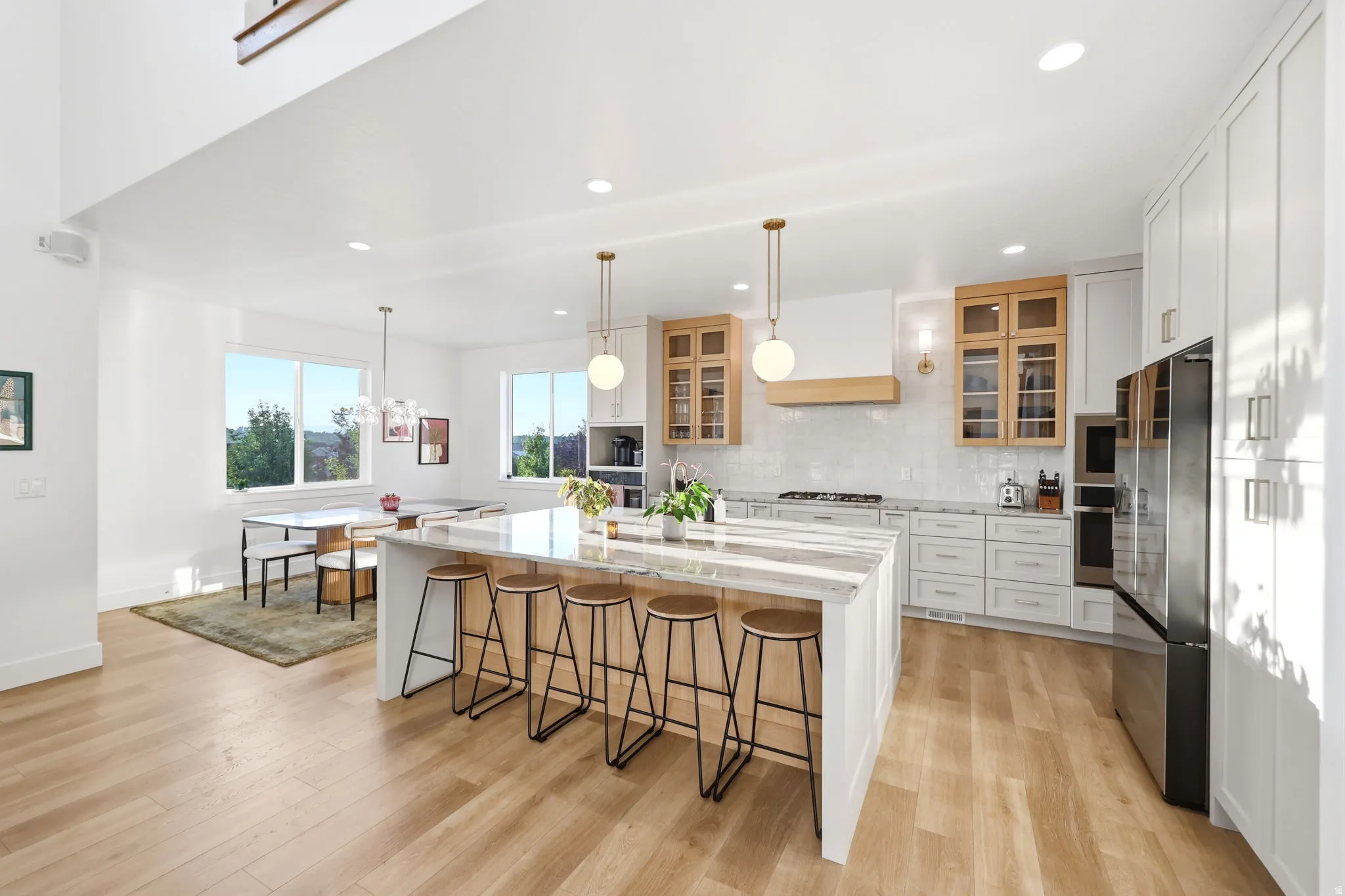 Expansive kitchen featuring a large island with countertop seating, light wood-finish flooring, white cabinetry, and stainless steel appliances