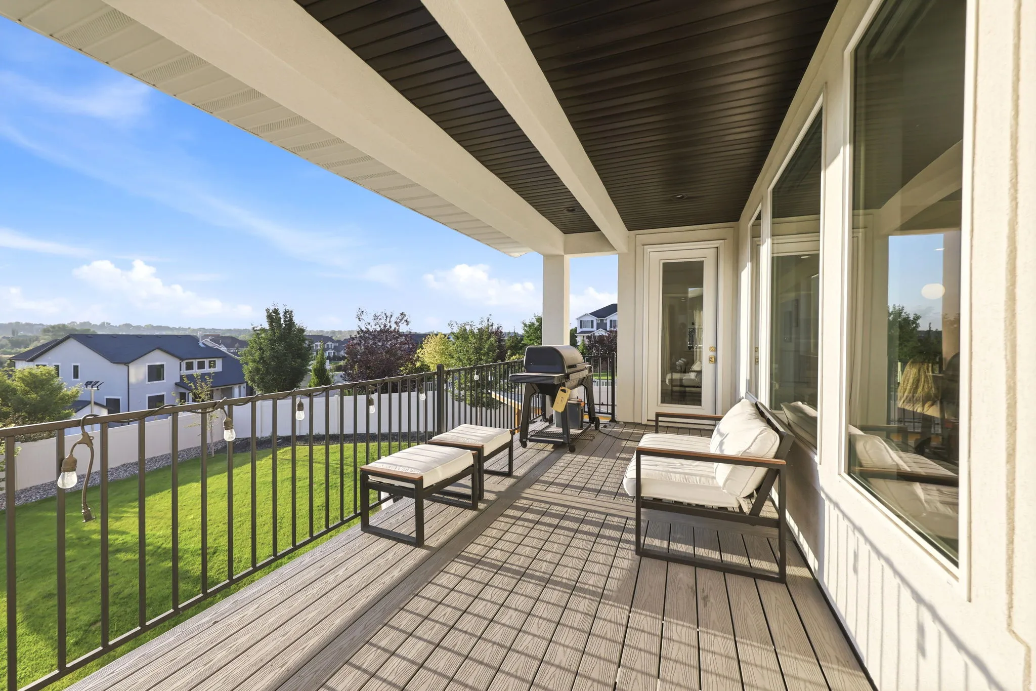 Elevated composite deck with black metal railings overlooking manicured lawn and mature landscaping