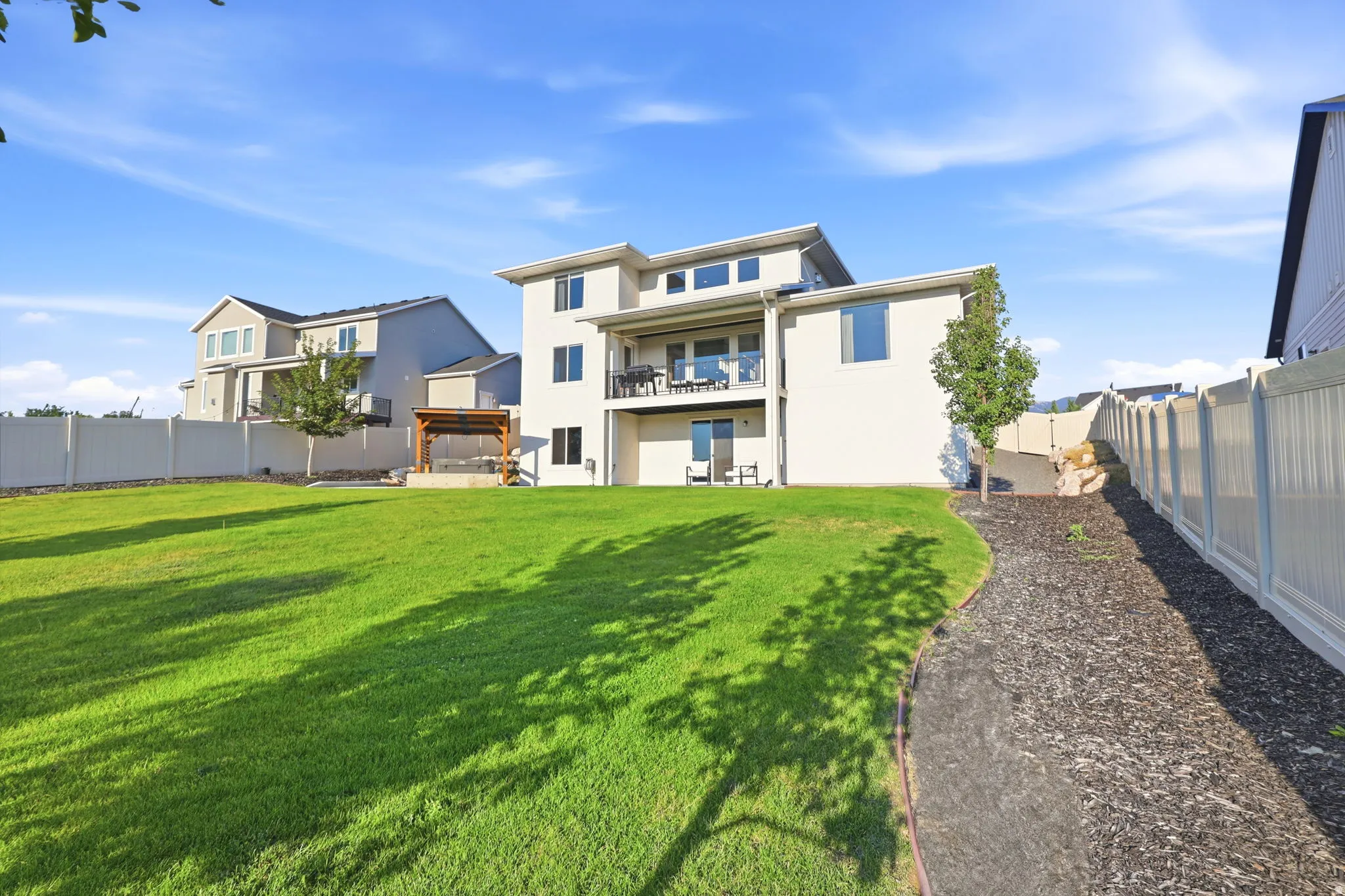 Expansive backyard featuring a manicured lawn with mature tree coverage, gravel pathway, and vinyl fencing