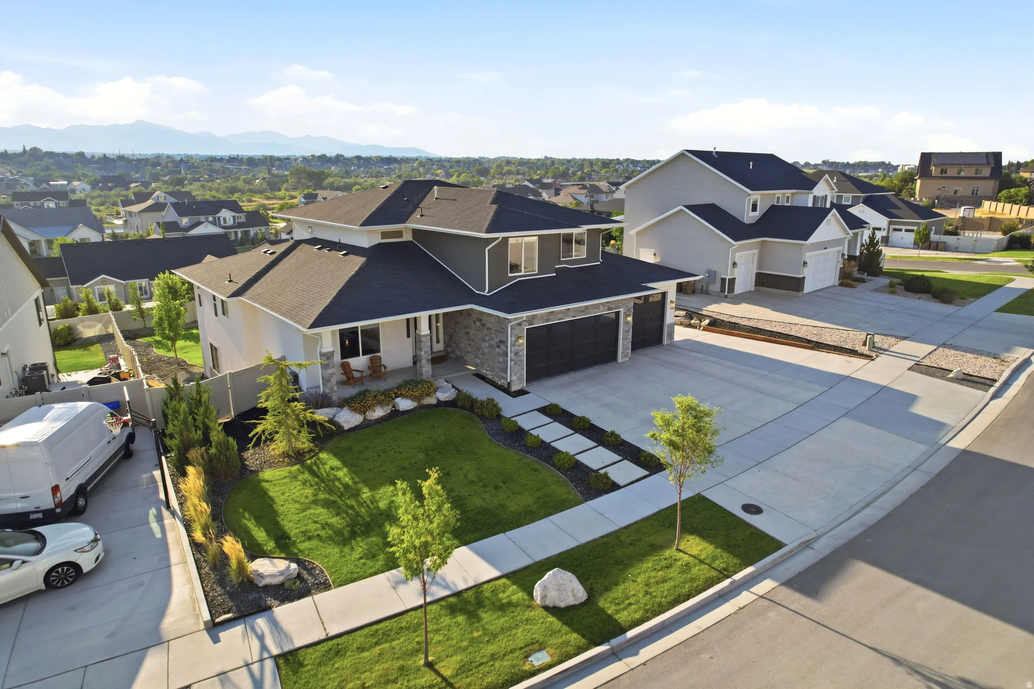 Contemporary two-story residence featuring a stone and stucco exterior, an attached three-car garage, a well-maintained front lawn with mature landscaping, and a concrete driveway