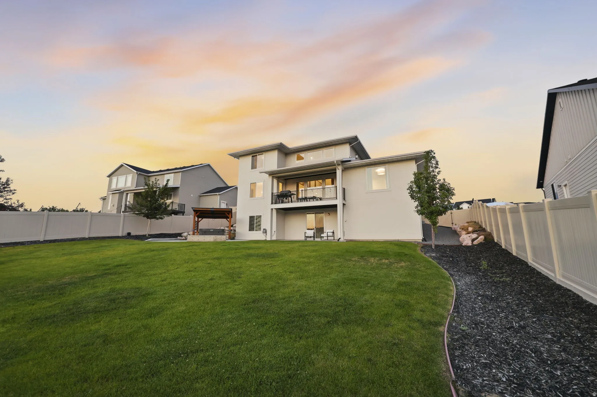Modern two-story residence showcasing a spacious rear elevation with clean architectural lines, multi-level deck with metal railings, manicured lawn, mature landscaping, and vinyl privacy fencing along the perimeter