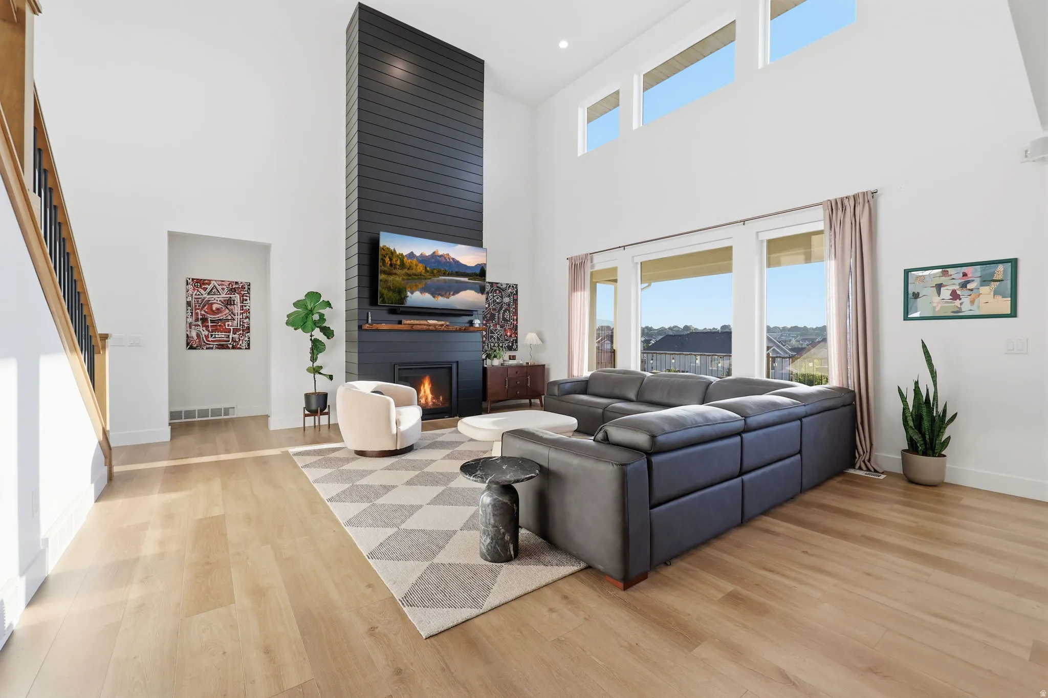 Soaring living room showcasing a dramatic two-story vaulted ceiling with clerestory windows, wide-plank wood-finish flooring, and a striking black linear fireplace with integrated media niche