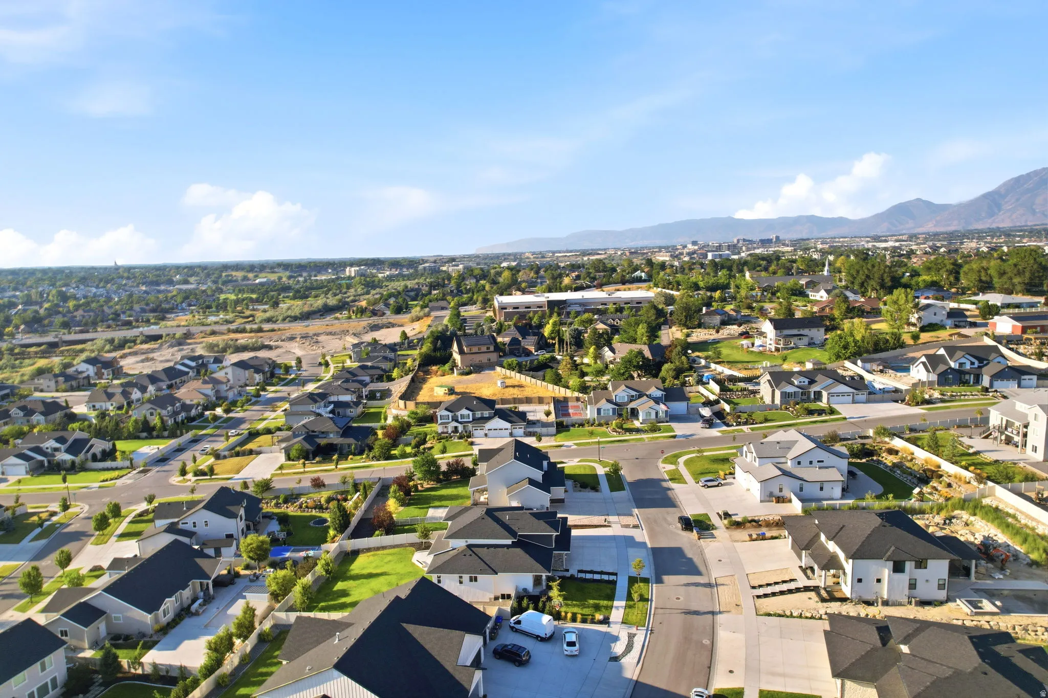 Aerial view showcasing a well-established residential community with contemporary homes featuring dark rooflines, manicured landscaping, and mature tree coverage