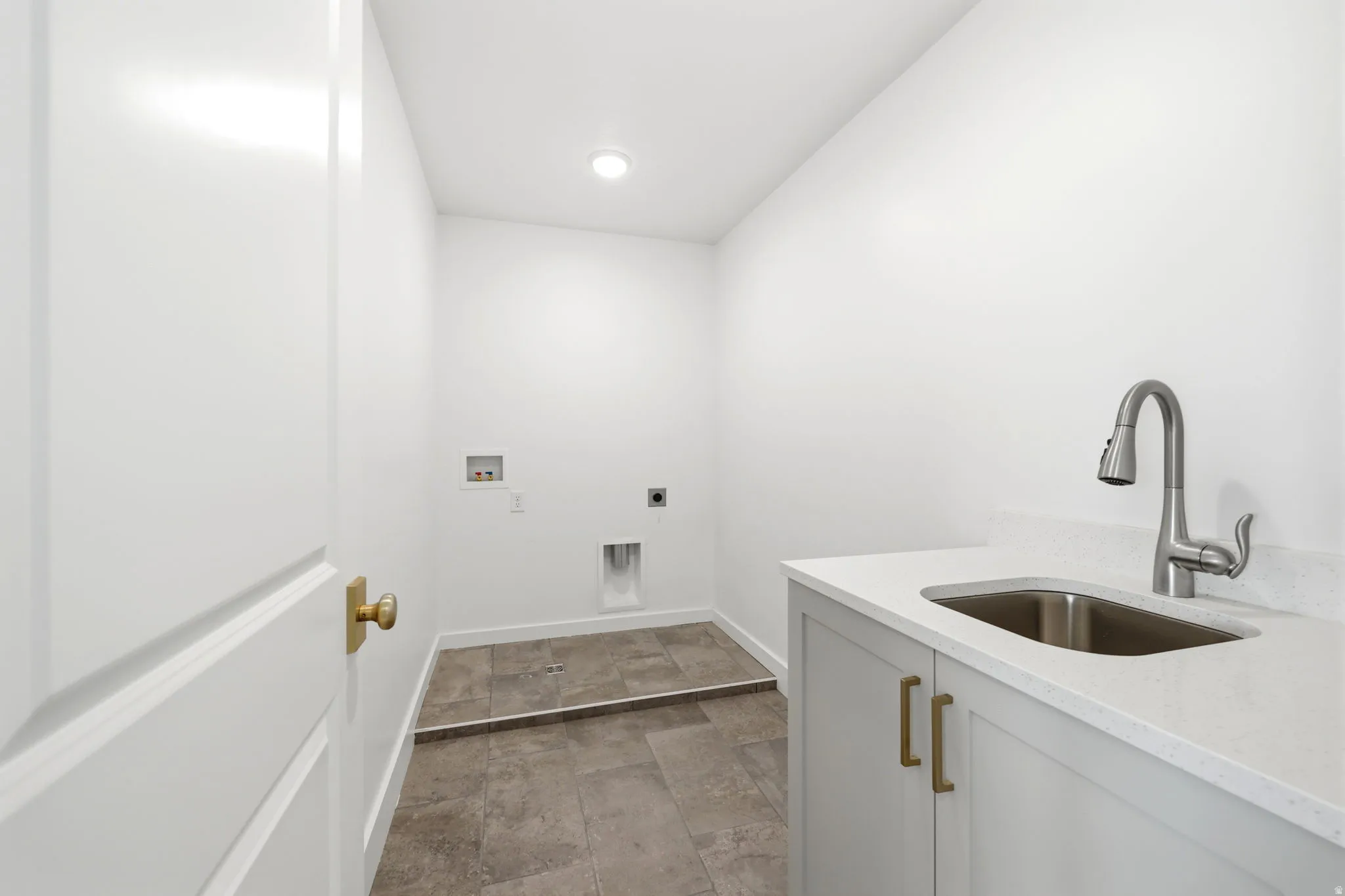 Modern utility kitchen featuring white cabinetry with brushed gold hardware, a stainless steel undermount sink, and a polished chrome pull-down faucet