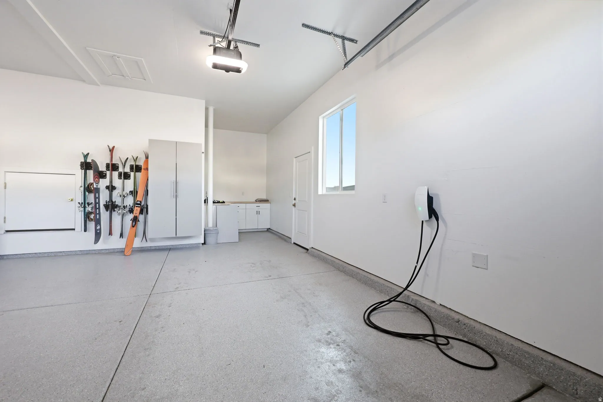 Spacious garage featuring polished concrete flooring, abundant natural light from high windows, wall-mounted tool organization system, and overhead ceiling-mounted fixtures