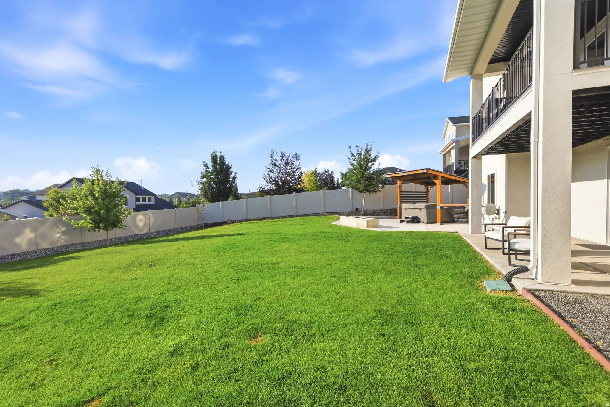 Expansive backyard featuring a lush, manicured lawn with mature landscaping and a white vinyl privacy fence