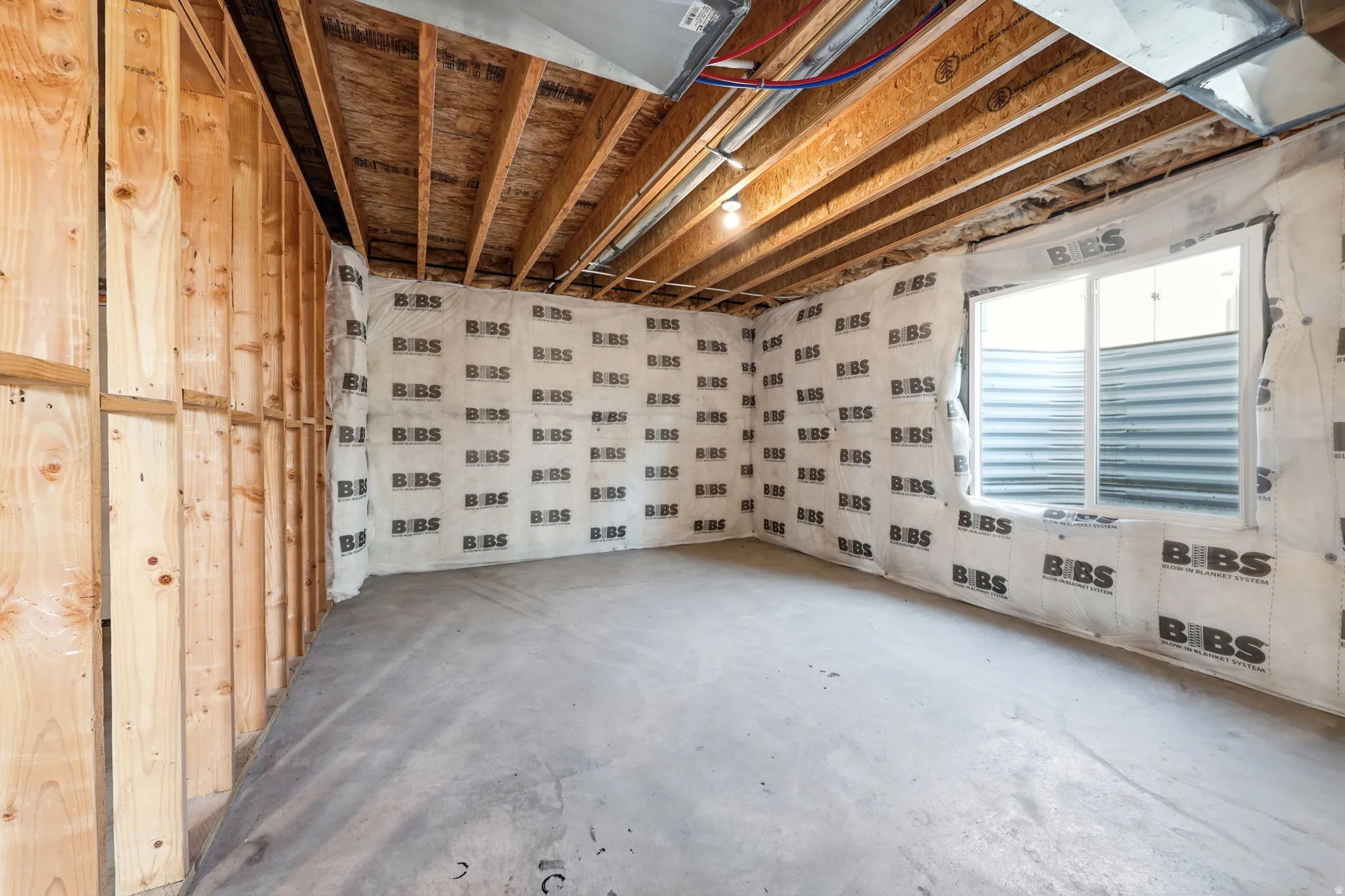 Unfinished interior space featuring exposed wooden beam ceiling with recessed lighting, concrete flooring, and white sheathing on walls