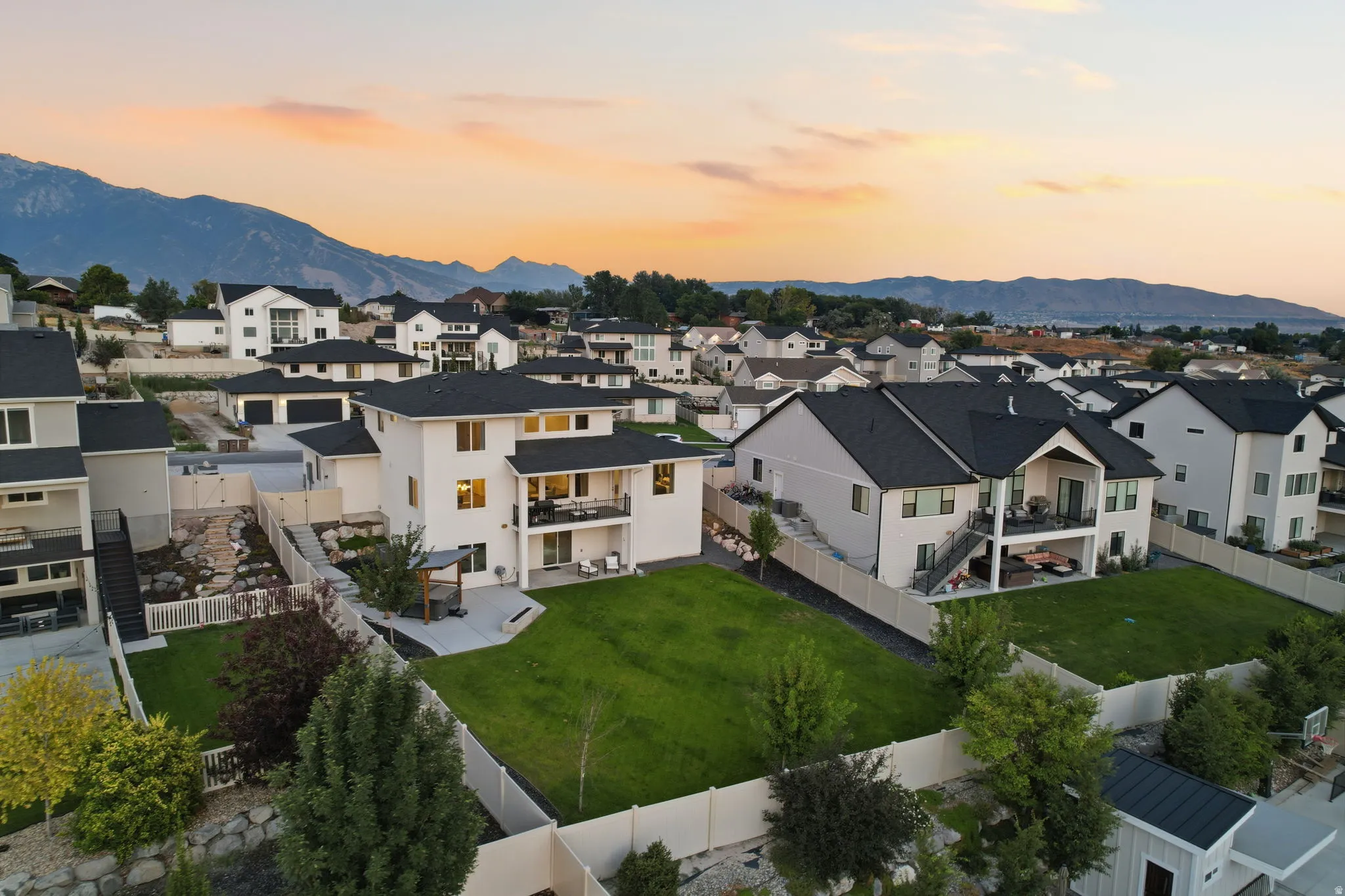 Expansive backyard featuring a large green lawn, concrete patio, and upper-level balcony