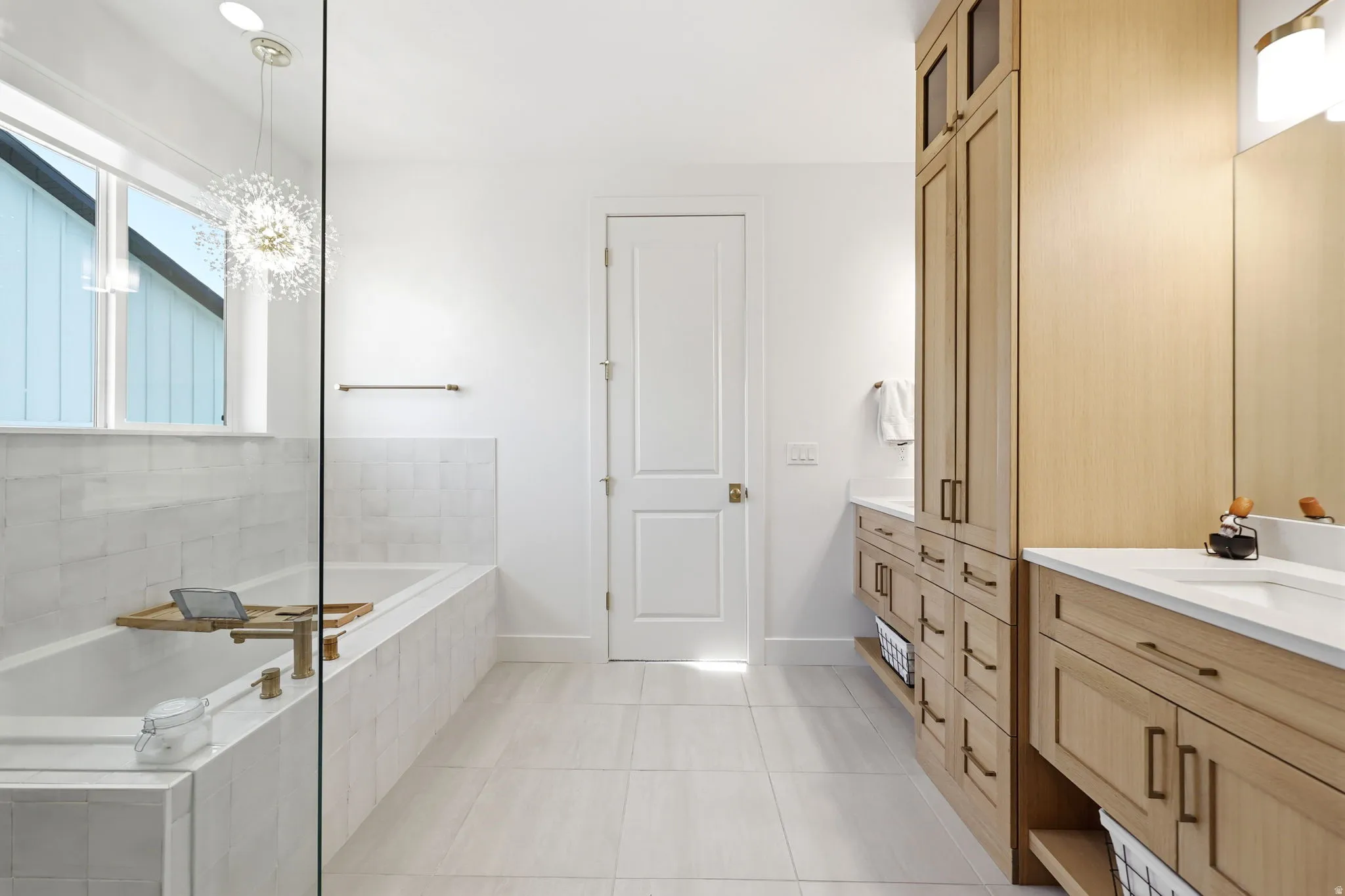 Spa-inspired primary bathroom featuring a soaking tub with glass enclosure, dual vanity with wood-finish cabinetry and ample storage drawers, quartz countertops, and polished tile flooring throughout
