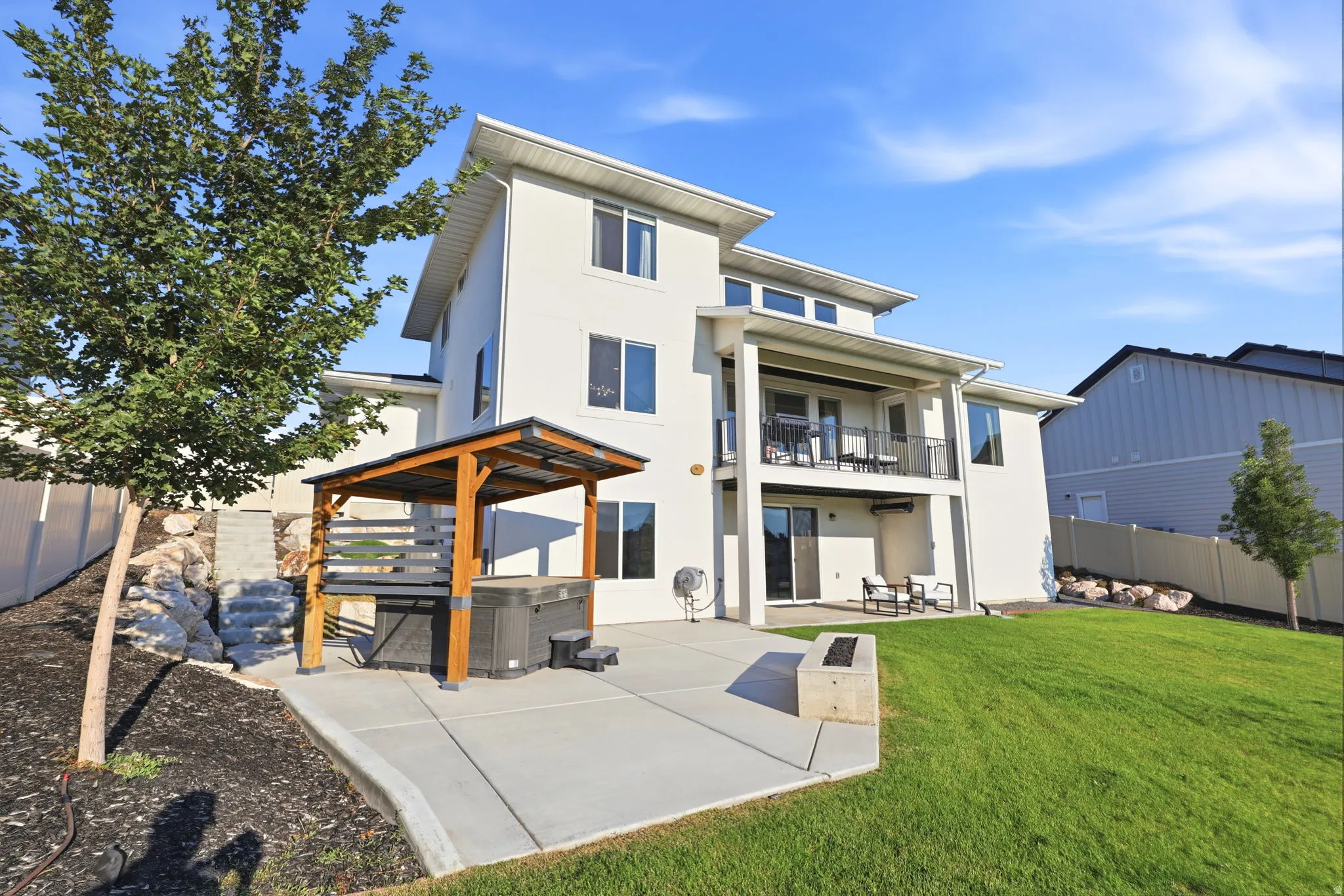 Modern three-story residence with clean-lined architecture, featuring a cream exterior, multi-level decking with metal railings, and a covered pergola structure