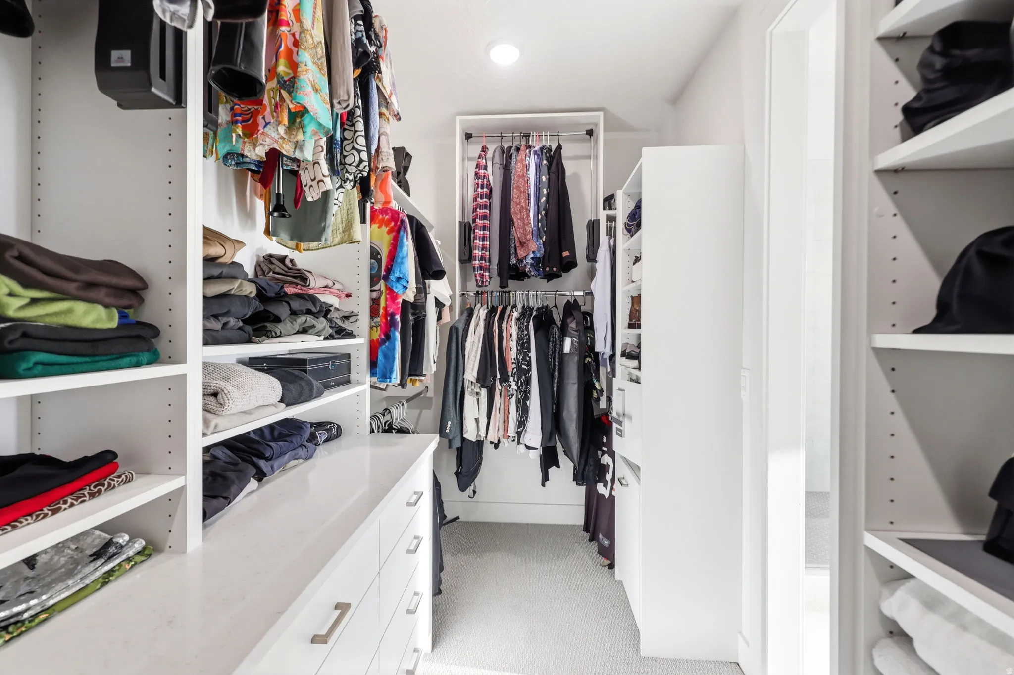 Custom walk-in closet featuring extensive built-in shelving with adjustable shelves, lower cabinetry with integrated storage, multiple hanging rods for garment organization, and strategic overhead lighting