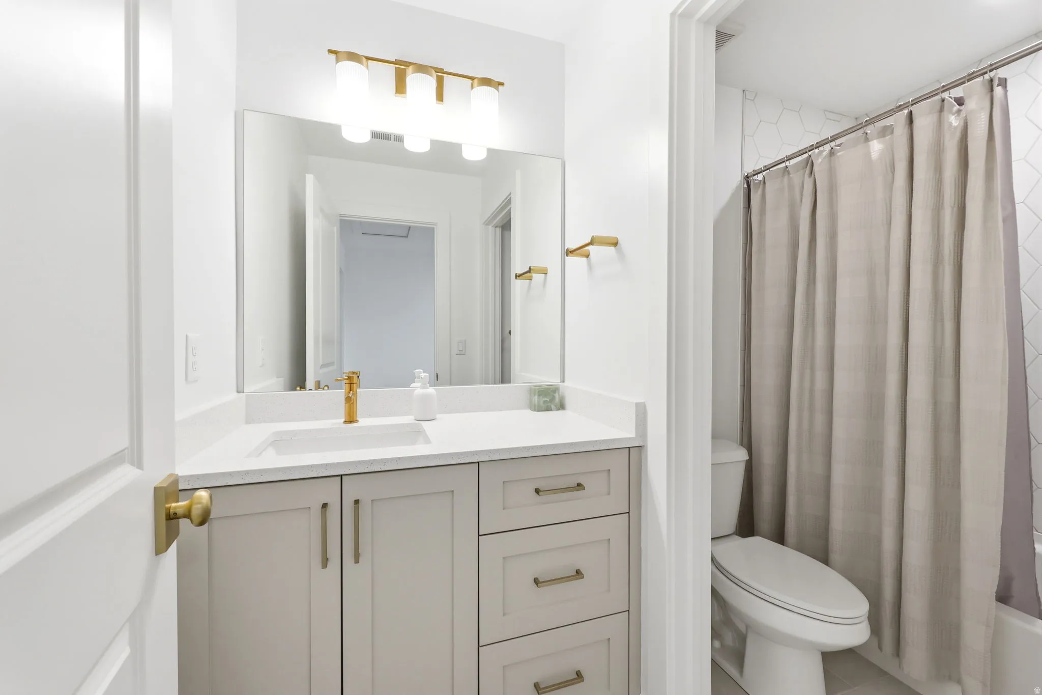 Modern bathroom featuring a custom vanity with soft-finish cabinetry, white quartz countertop, and brushed gold hardware