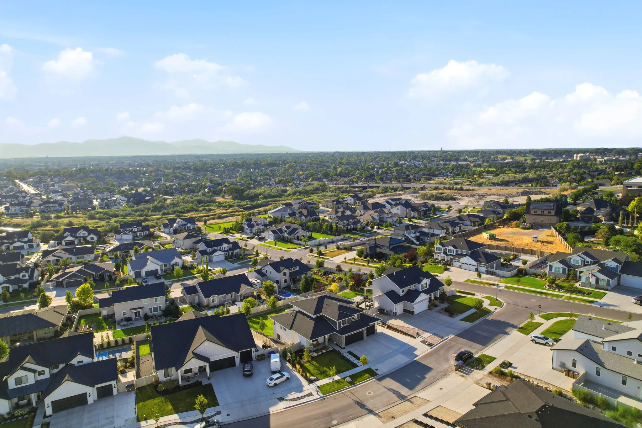 Aerial view showcasing a well-established residential community with contemporary homes featuring dark architectural rooflines, manicured lawns, and mature landscaping throughout the neighborhood