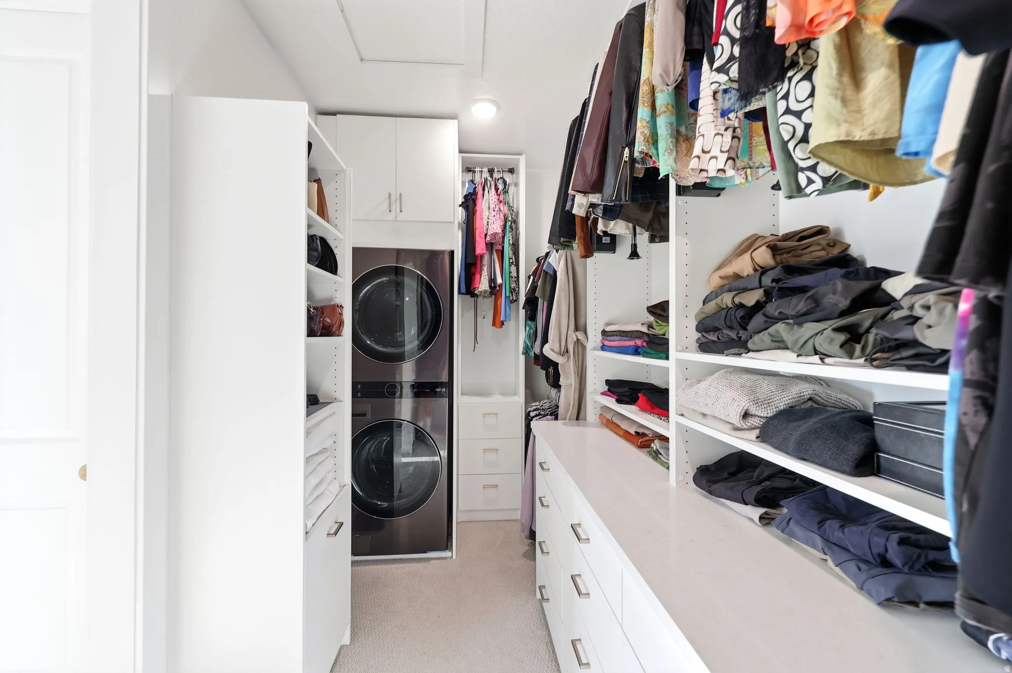 Spacious walk-in closet featuring custom white cabinetry with multiple shelves and drawers, integrated clothing rods with organized hanging storage, and abundant natural lighting from recessed ceiling fixtures