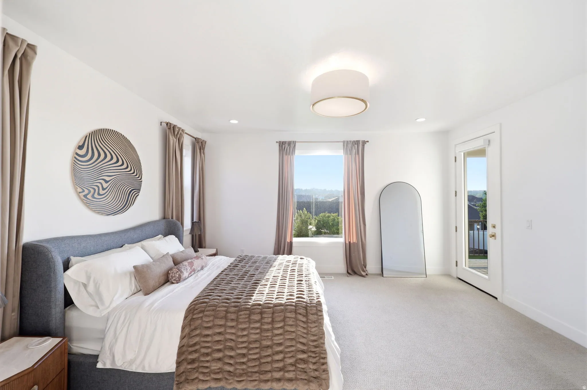 Spacious primary bedroom featuring a gray upholstered bed frame, neutral carpet flooring, and recessed ceiling lighting