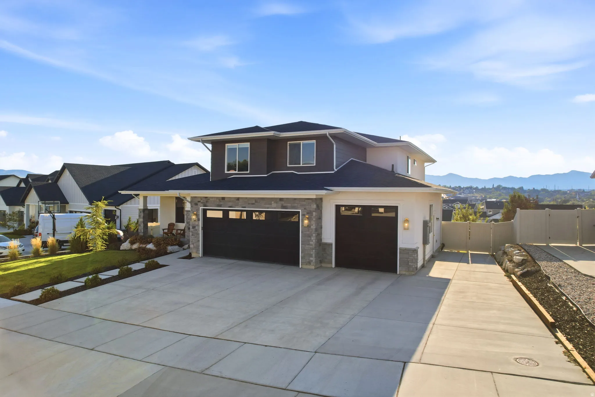 Contemporary two-story residence featuring a combination of stone and stucco siding, a multi-car garage with dark paneled doors, a concrete driveway, and a landscaped front yard with a stepping stone pathway