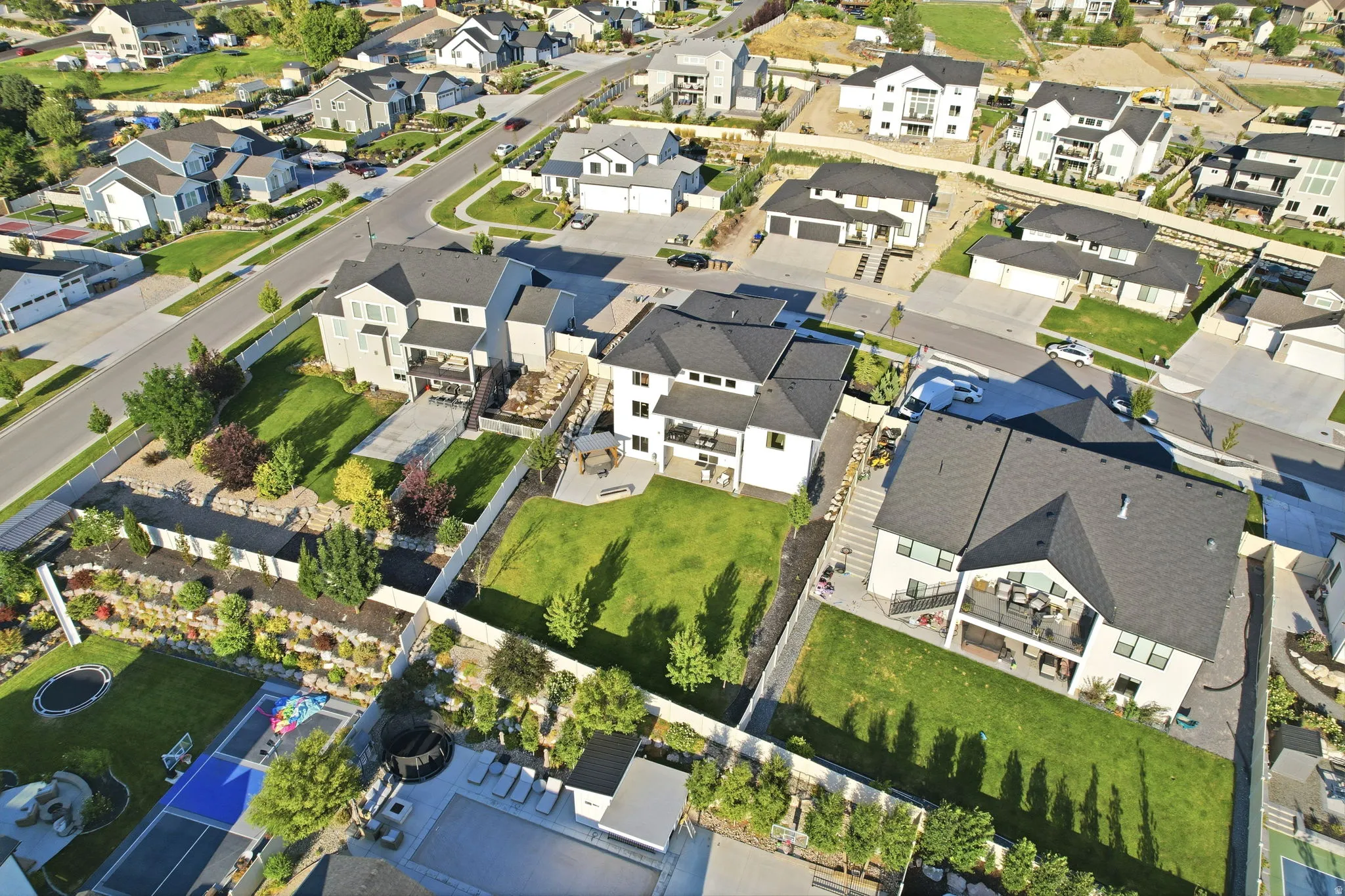 Aerial view showcasing a modern residence with clean architectural lines, featuring a dark-toned roof, white exterior walls, and a substantial manicured lawn
