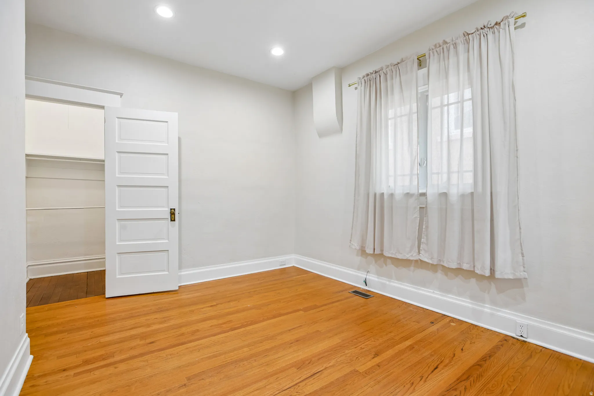 Hardwood flooring throughout featuring recessed lighting, a closet with built-in shelving, a large window, and white trim
