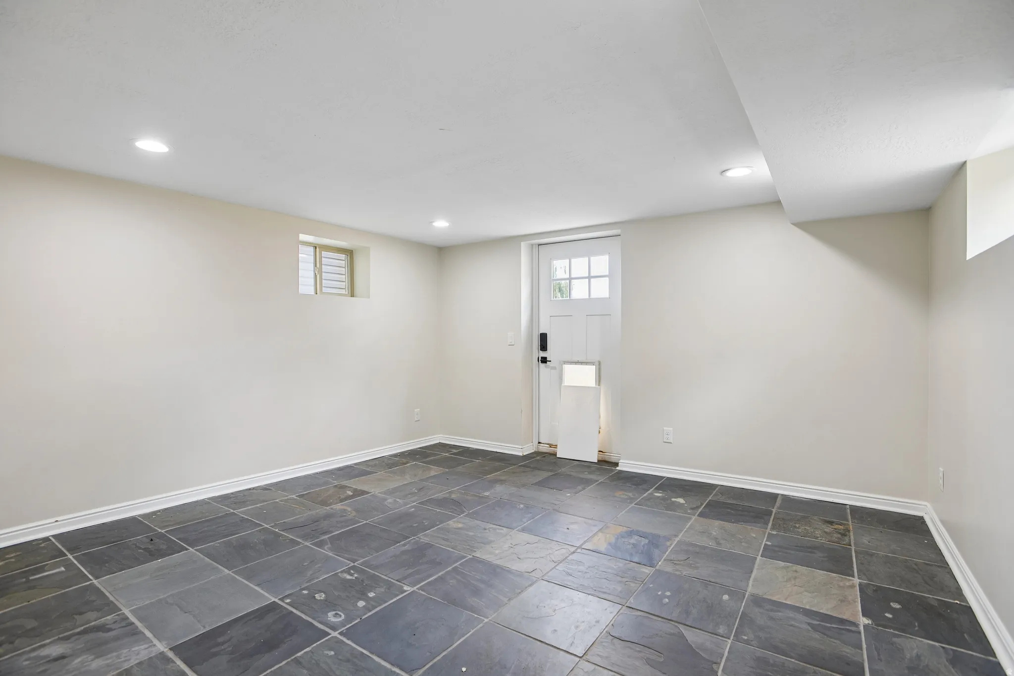 Substantial room featuring large format slate floor tiles, recessed lighting, neutral wall tones, and a paneled exterior door with glass lites