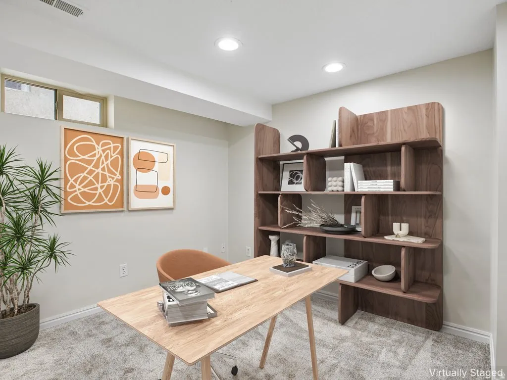 Recessed lighting illuminates this versatile space featuring light gray walls, plush carpeting, and a built-in wood-finish shelving unit