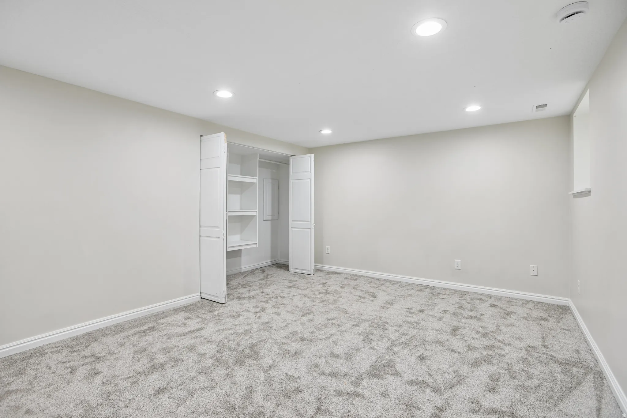 Spacious room featuring light gray walls, plush gray carpeting, white baseboards, and ceiling-mounted recessed lighting