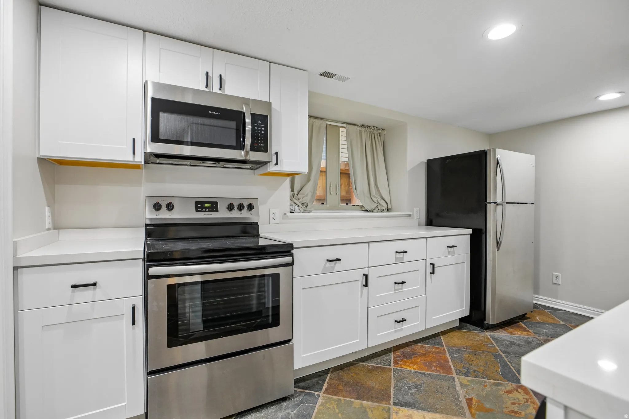 Kitchen featuring stainless steel appliances, white cabinetry, solid surface countertops, recessed lighting, and a multi-toned slate-look floor