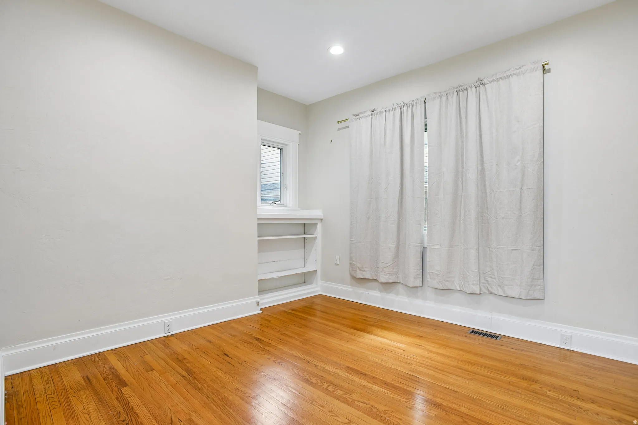 Room with wood-finish flooring, light-colored walls, and a recessed ceiling light