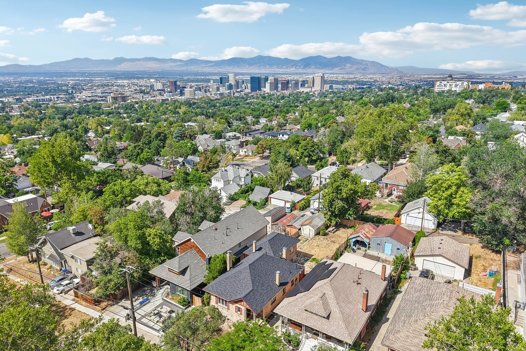 Aerial perspective showcasing a residential neighborhood with a distant cityscape and mountains under a blue sky with scattered clouds