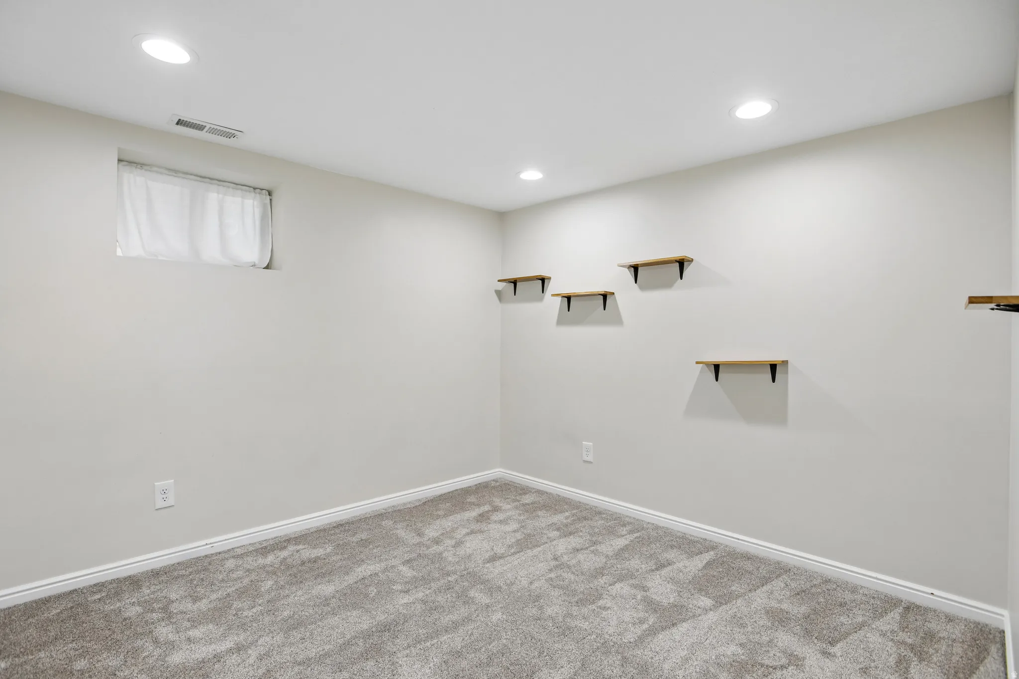 Neutral-toned carpeting complements light gray wall finishes in this room, featuring recessed ceiling lighting
