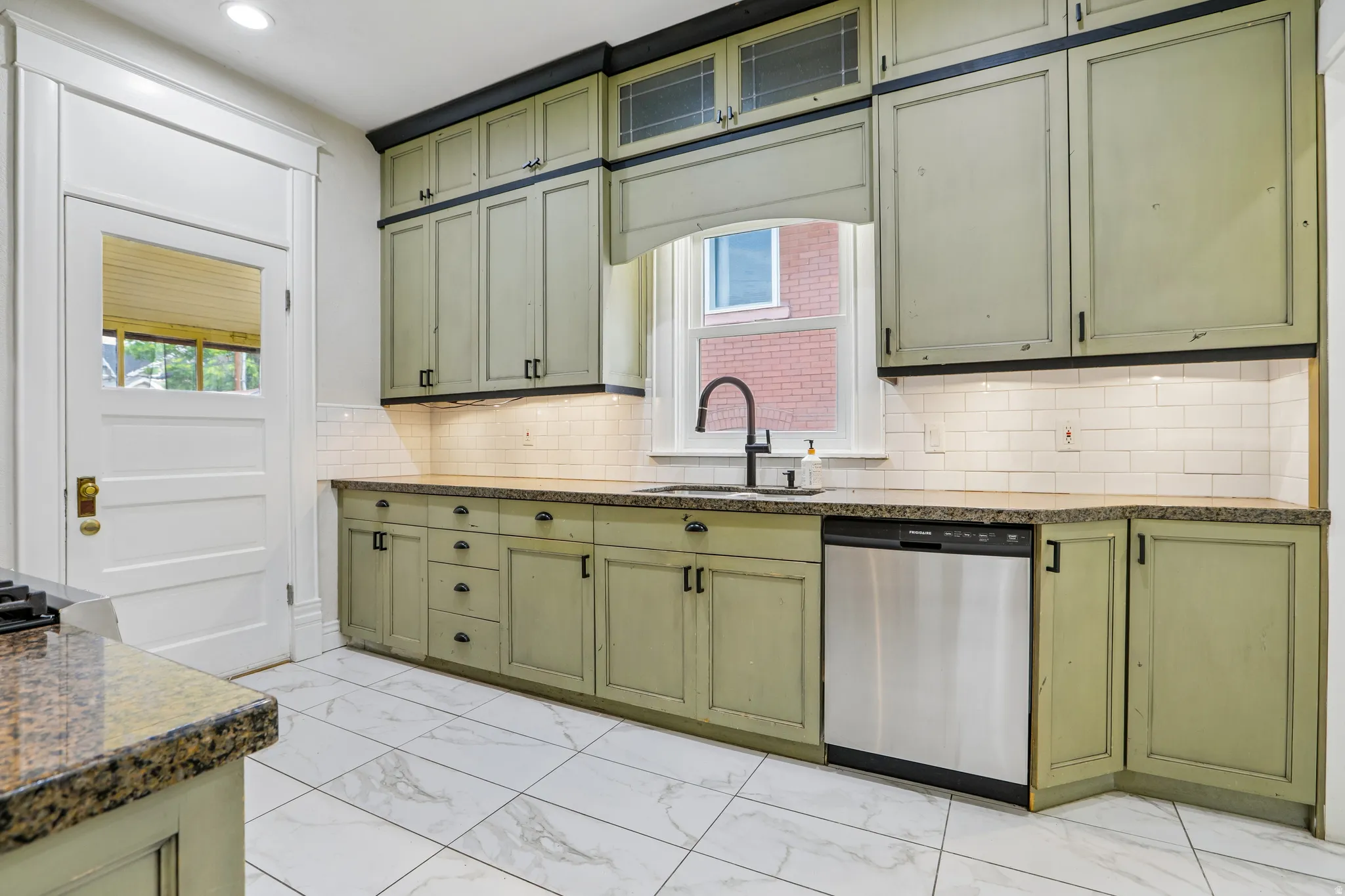 Kitchen featuring wood-finish cabinetry, stone-finish countertops, white subway tile backsplash, and stainless steel dishwasher