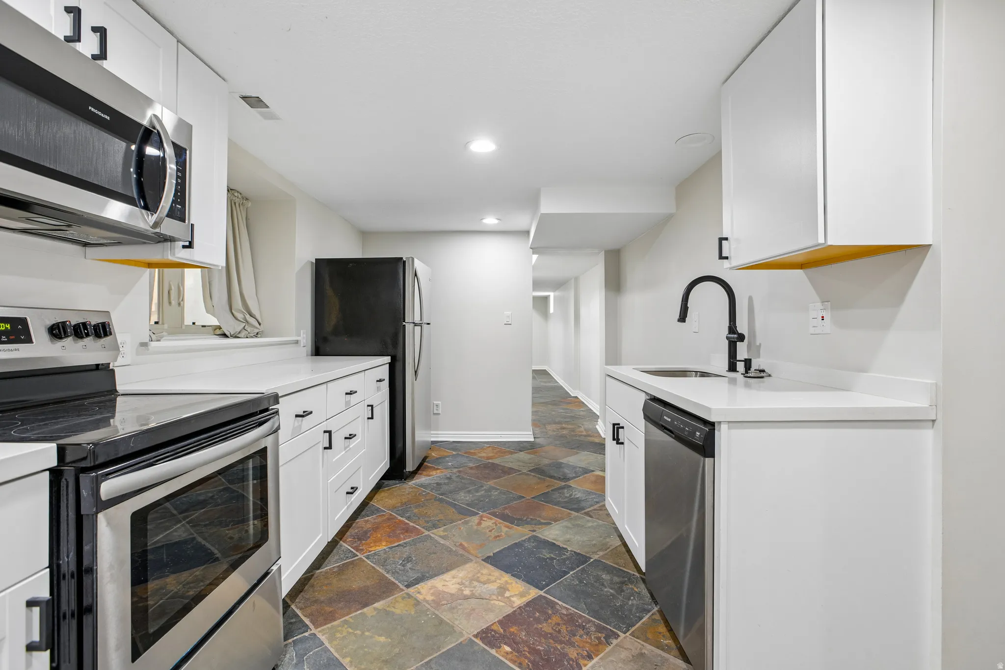 Modern kitchen featuring white cabinetry, stainless steel appliances, light countertops, and multi-toned tile flooring