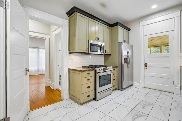 Kitchen featuring stainless steel appliances, granite-style countertops, subway tile backsplash, and light wood-finish cabinetry with dark crown molding