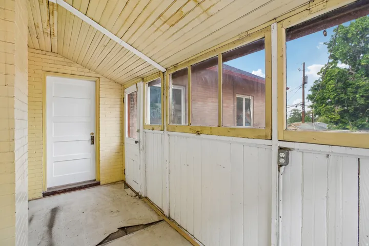 Enclosed porch featuring a slatted wood ceiling, painted brick wall, white paneled doors, multiple windows, and a concrete floor