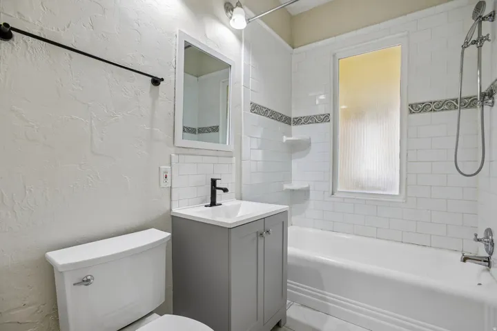 Bathroom featuring a white subway tile surround, a bathtub with a shower system, and a vanity with a matte black faucet