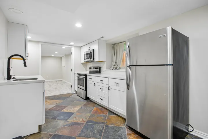 Kitchenette featuring multi-toned slate flooring, white cabinetry with black hardware, stainless steel appliances, and a white countertop with an undermount sink and matte black faucet