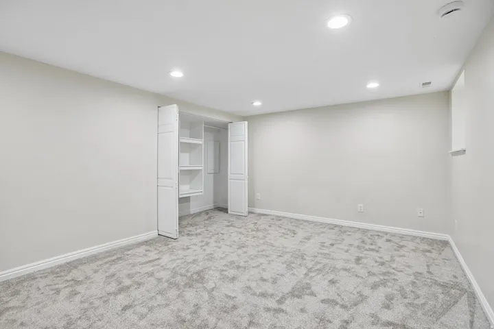 Spacious room featuring light gray walls, plush gray carpeting, white baseboards, and ceiling-mounted recessed lighting