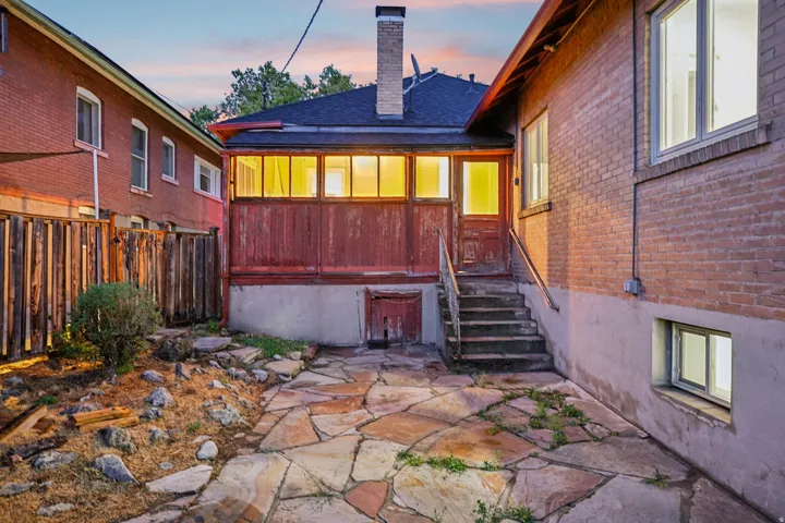 Rear exterior featuring a flagstone patio, brick siding, and a wood-paneled enclosed porch with an exterior staircase