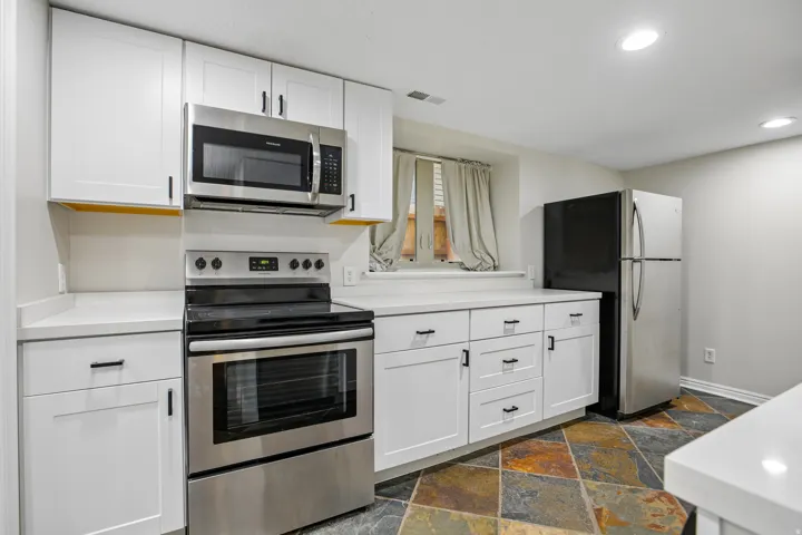 Kitchen featuring stainless steel appliances, white cabinetry, solid surface countertops, recessed lighting, and a multi-toned slate-look floor