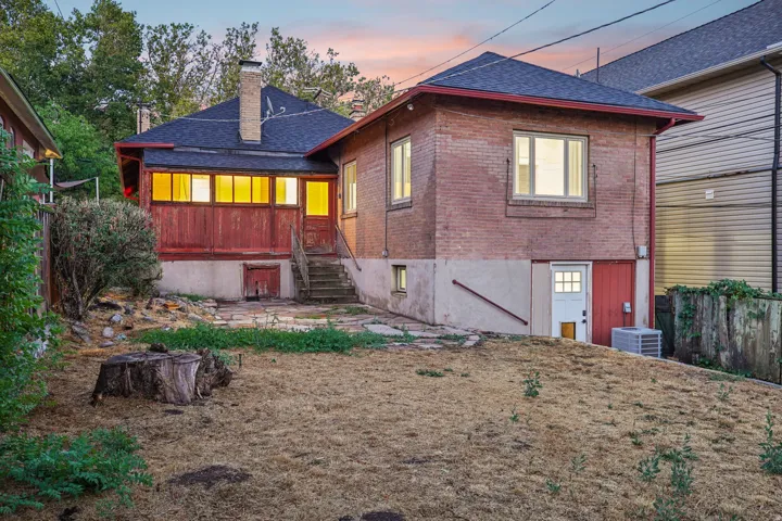 Brick exterior with a red-painted enclosed porch, lower-level entry, and a sloped yard