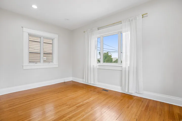 Bright interior space featuring wood-finish flooring, white baseboards, and two windows with white trim