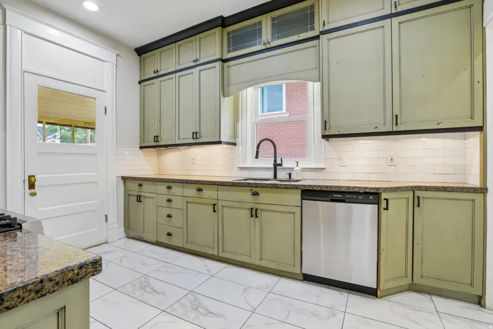 Kitchen featuring wood-finish cabinetry, stone-finish countertops, white subway tile backsplash, and stainless steel dishwasher