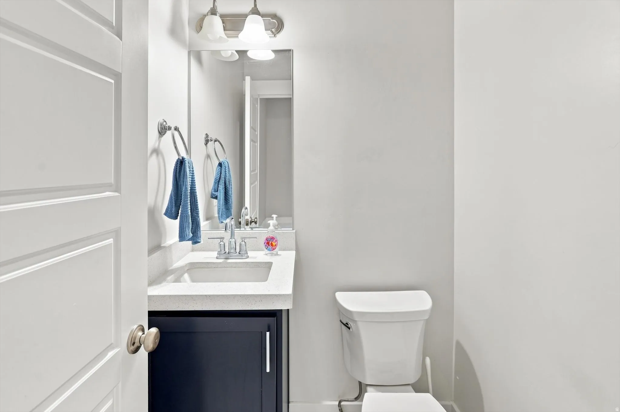 White door with brushed nickel hardware, built-in vanity with dark cabinetry, integrated sink, and wall-mounted mirror