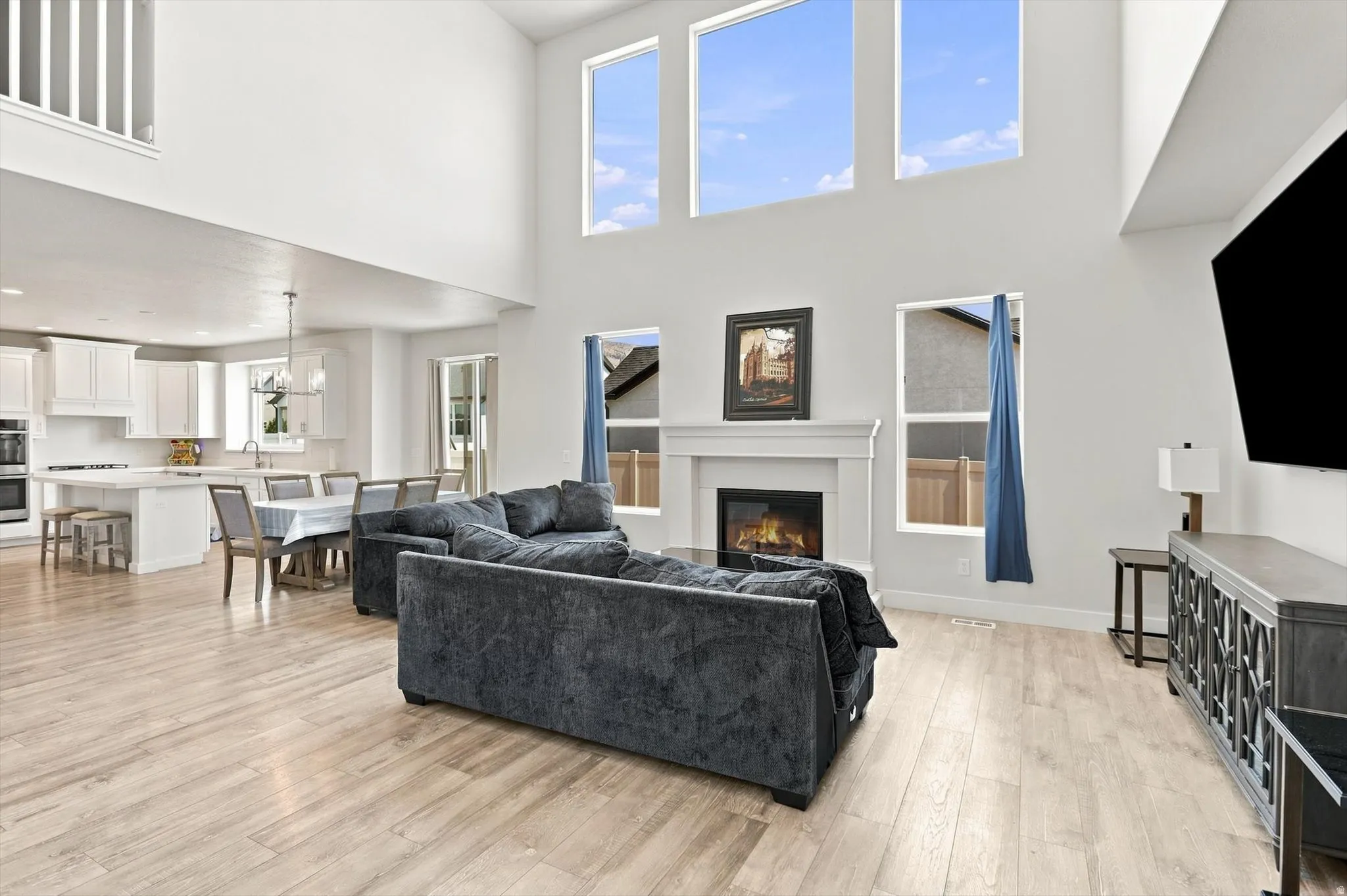 Vaulted living area featuring wood-finish flooring, a white mantel fireplace, and high windows