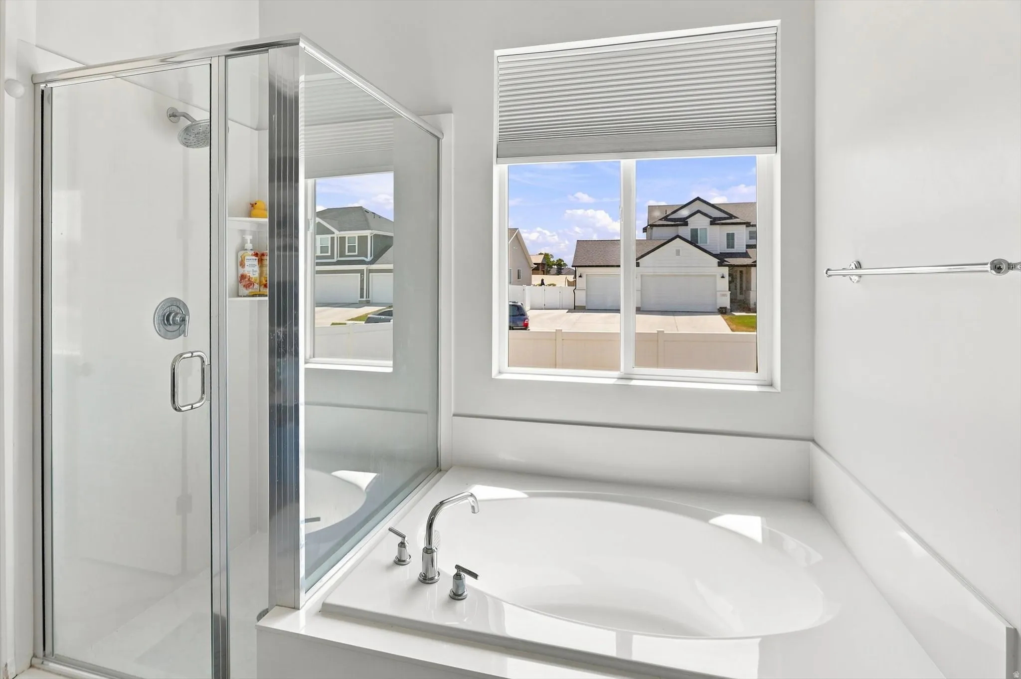 Glass-enclosed shower, built-in shower shelf, soaking tub, window with pleated blind, and polished chrome fixtures