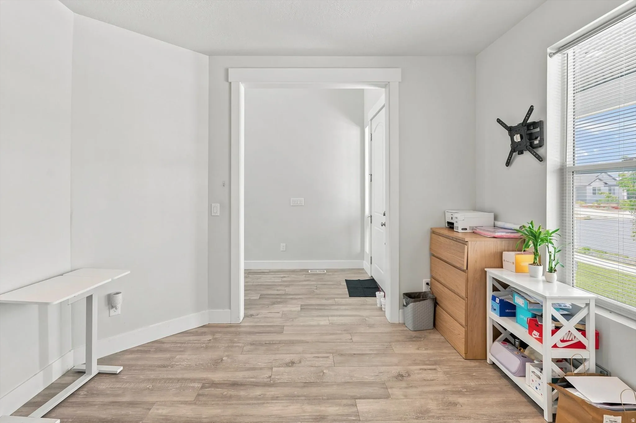 Bright, open room featuring wood-finish flooring throughout, white painted walls, and abundant natural light from large windows with blinds