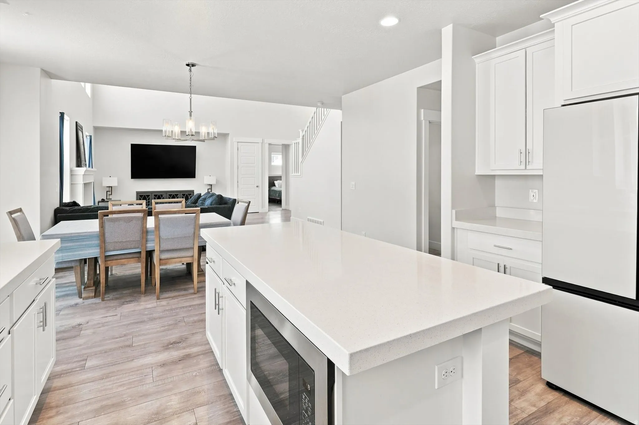 Modern kitchen featuring white cabinetry with integrated hardware, a large waterfall-edge island with white quartz countertop, stainless steel appliances including a built-in microwave, and wood-finish flooring throughout