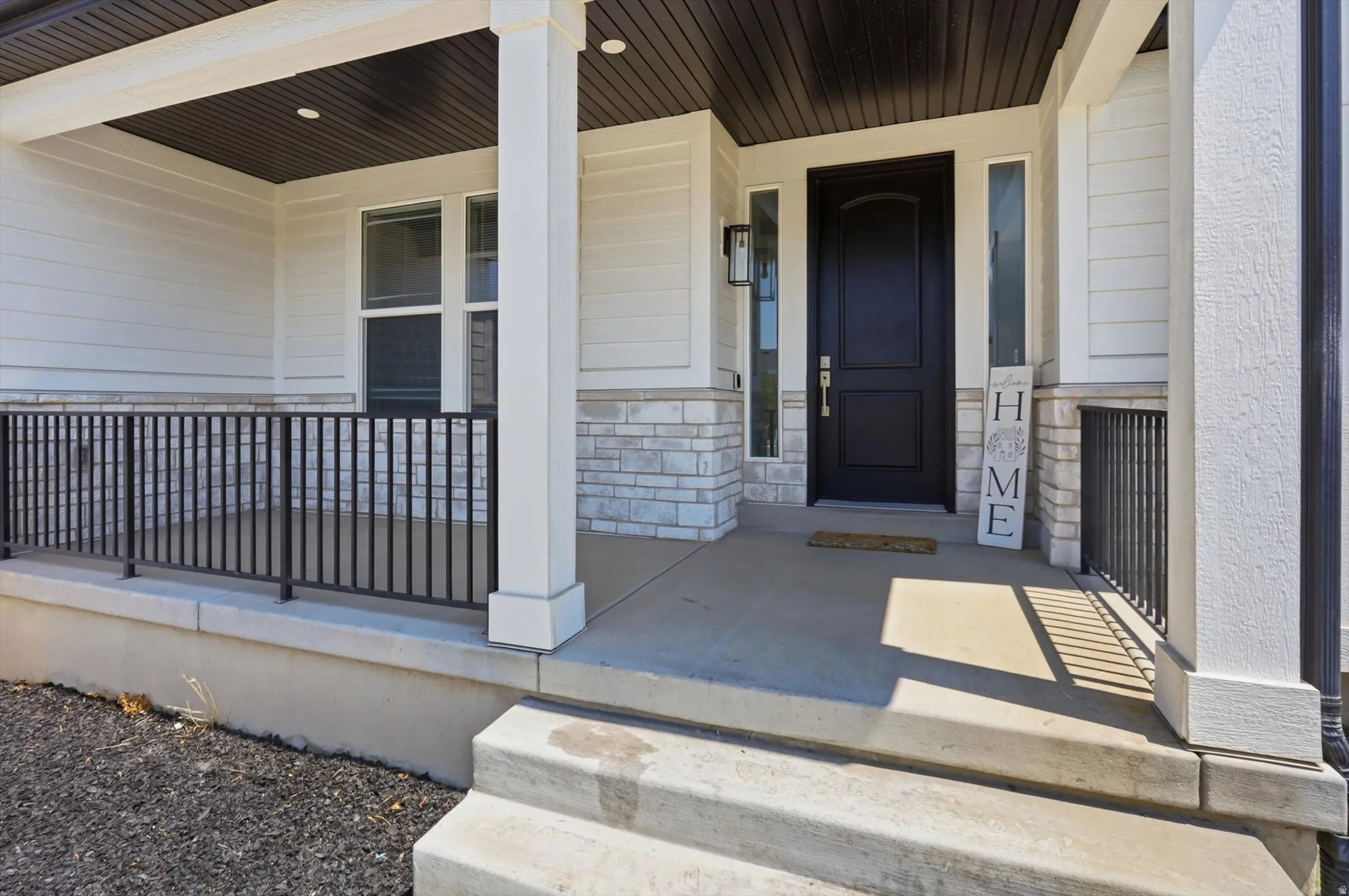 Welcoming front porch featuring white composite columns, metal railing with vertical spindles, and a covered ceiling with dark wood-finish soffit
